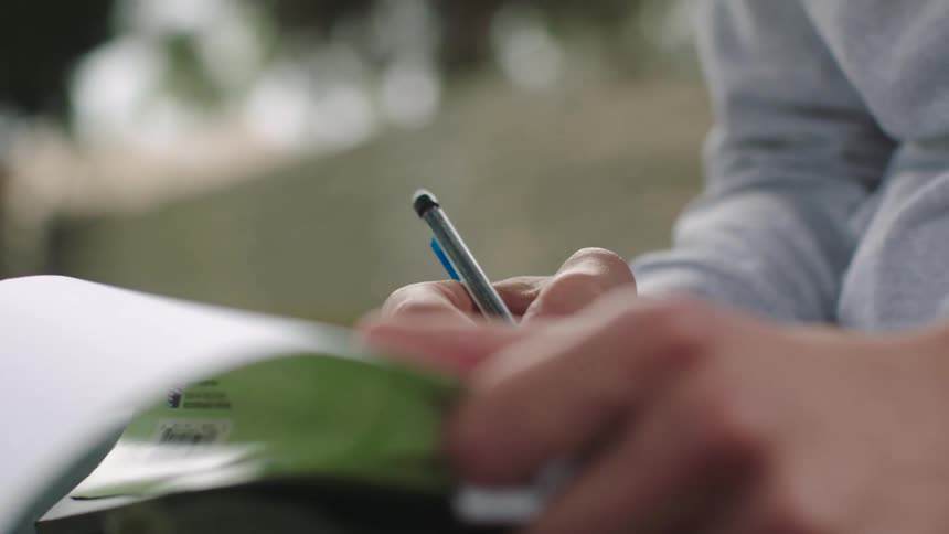 A person is writing in a pad with a pencil outside
