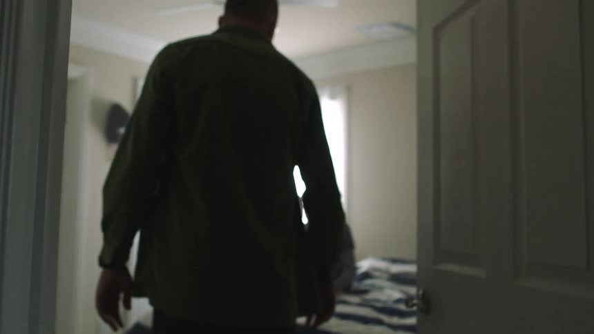 Father angrily opens a bedroom door and walks towards his son who is sitting on the bed looking sad