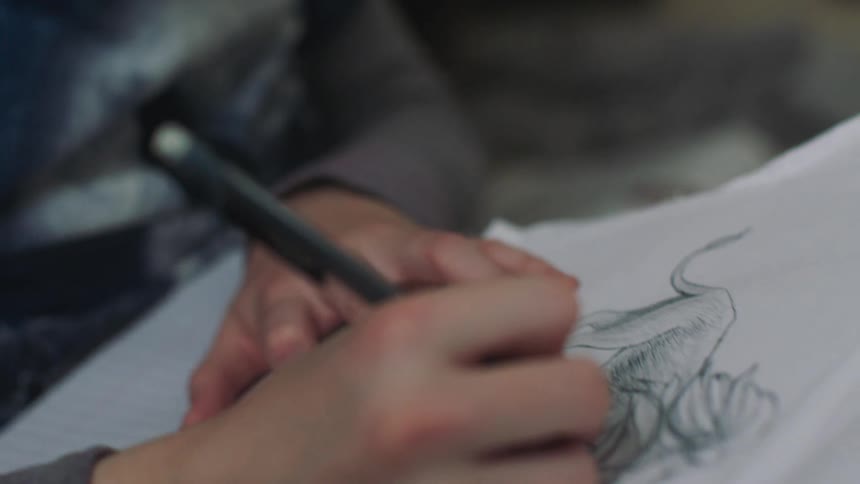 Teenaged boy draws a sketch on white paper
