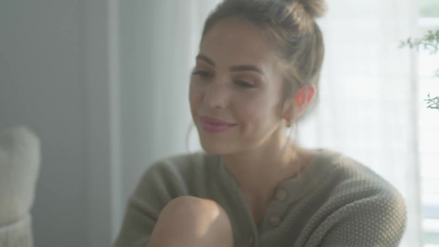 A woman sitting hugging her knee swaying to music and looking in love