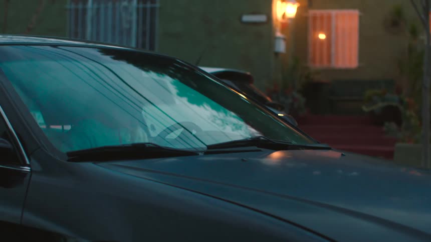 Woman sits in the passenger seat of a car as a man drives it in reverse while backing up then drives down the street