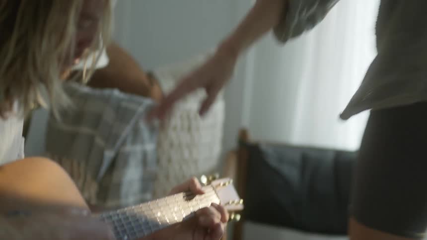 Man plays a guitar as his girlfriend watches then she gets up and takes his hand and they walk away