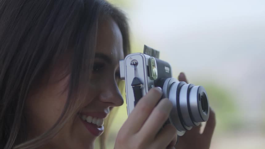 A woman is taking a picture and she holds the photograph when it comes out of the camera