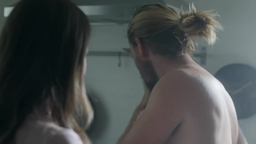 Woman feeds her boyfriend food on a spoon while they stand in the kitchen