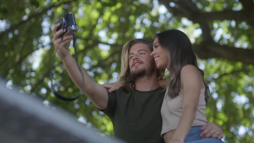 Man and woman under a tree as the man holds up a camera and takes a photo of the both of them