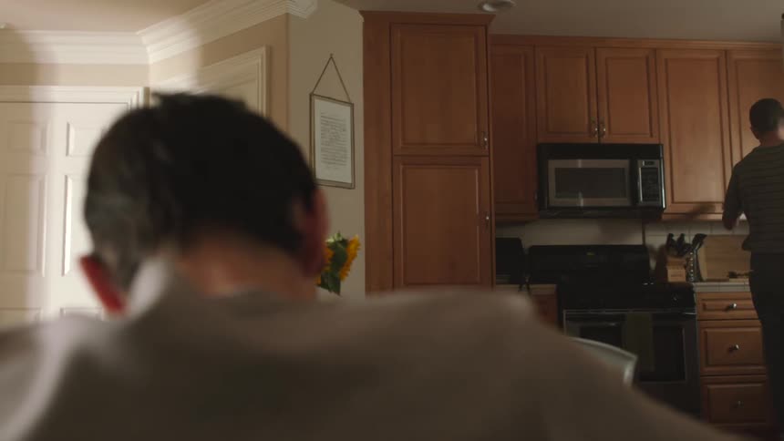 A man looks at his son sitting at the kitchen table and opens a cabinet