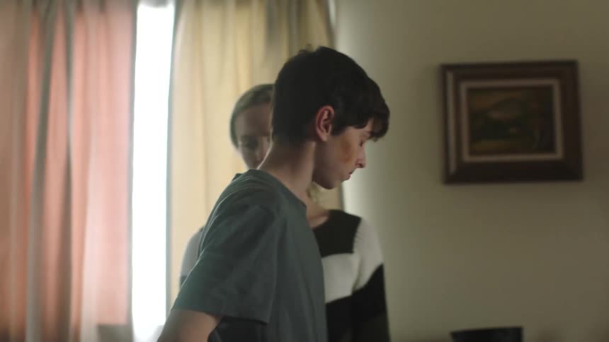 Son pushes himself up from the chair and away from the table and walks away from his mother and they both look sad