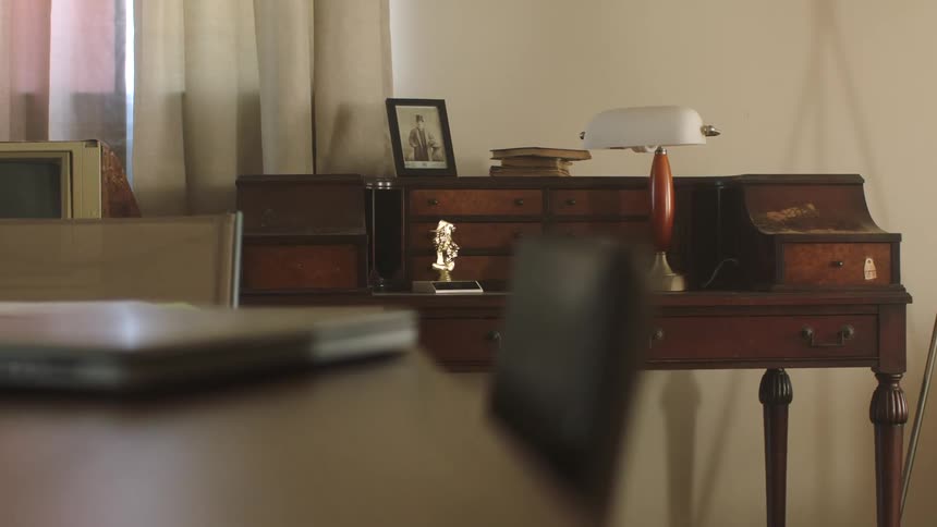 A closed laptop on a table with a writing desk against the wall