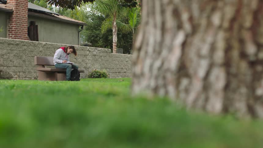 A man is writing on the park bench
