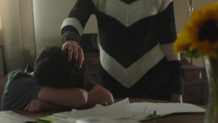 A woman walks through her house and finds her son sleeping with his head on the table and she picks up a drawing and looks at it