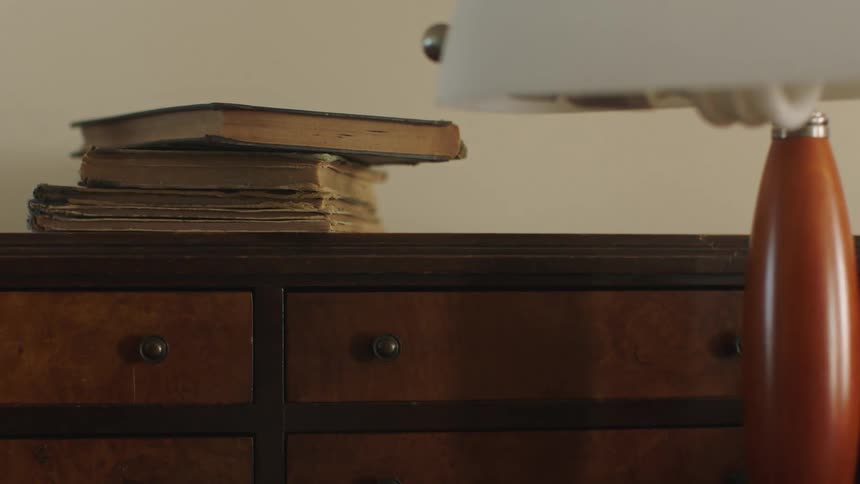 Pile of books sit on a cabinet as a lamp sits in front of it