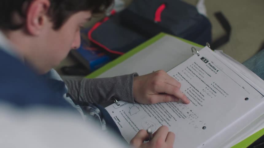A boy sitting on the floor doing his homework in a workbook