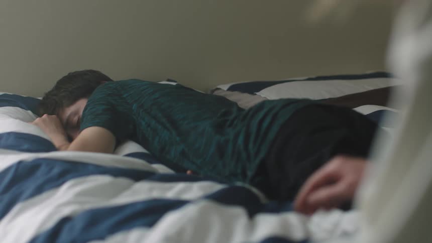 Woman touches males leg as he lies sleeping on his stomach on a bed