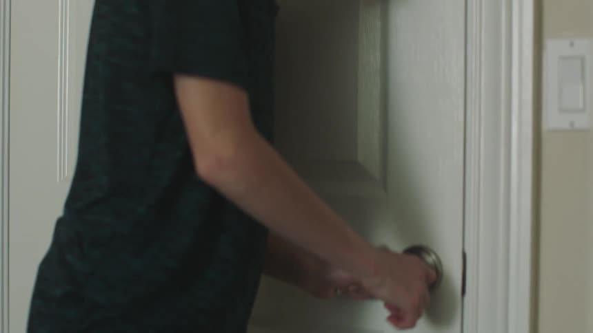 A boy runs into his room and locks the door quickly looking sad and anxious