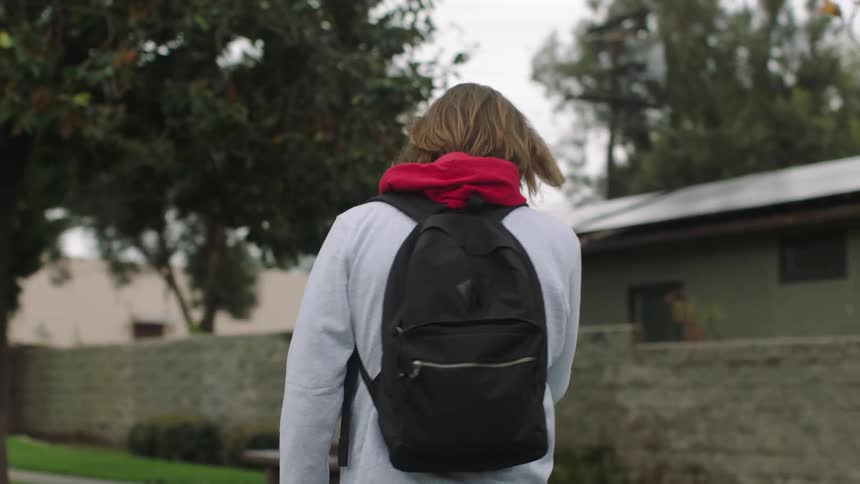 Man enters park and walks along sidewalk with house in the background