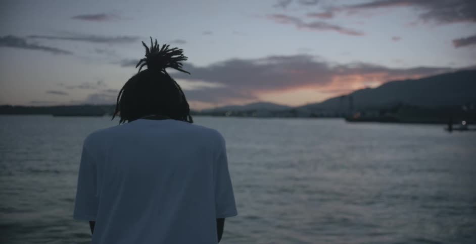 A man is standing by the water at sunset