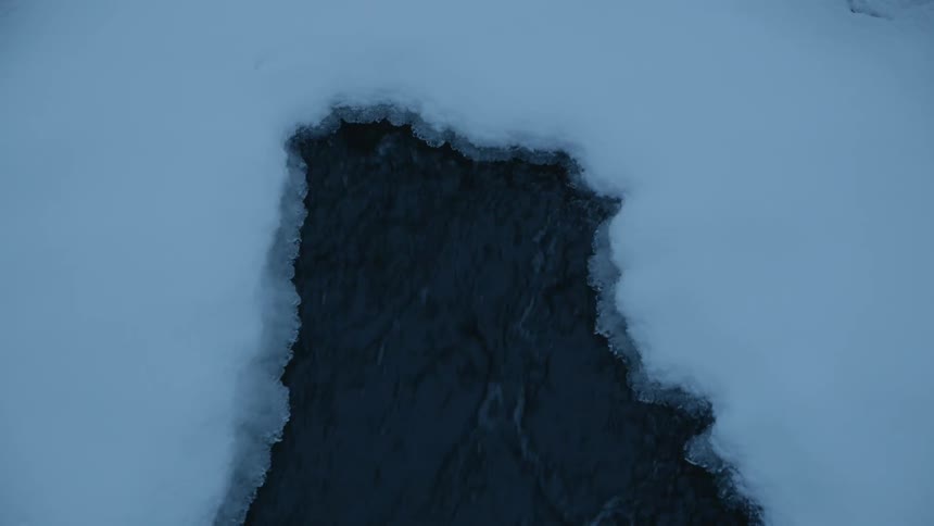 A fast moving river breaks off pieces of snow and ice above it
