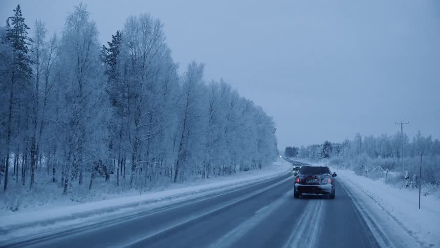 Vehicles travel along a road through a snowy countryside in the evening