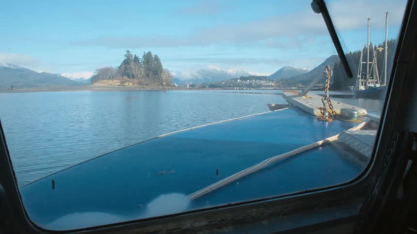 Boat travels on the lake past a docked sailboat under a blue sky as mountains sit in the distance