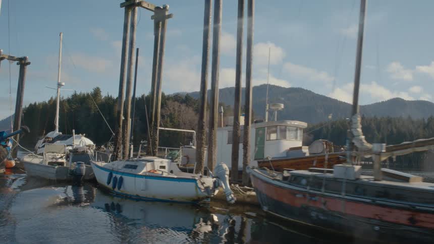 Floating past fishing boats sit docked along a pier near a mountain range