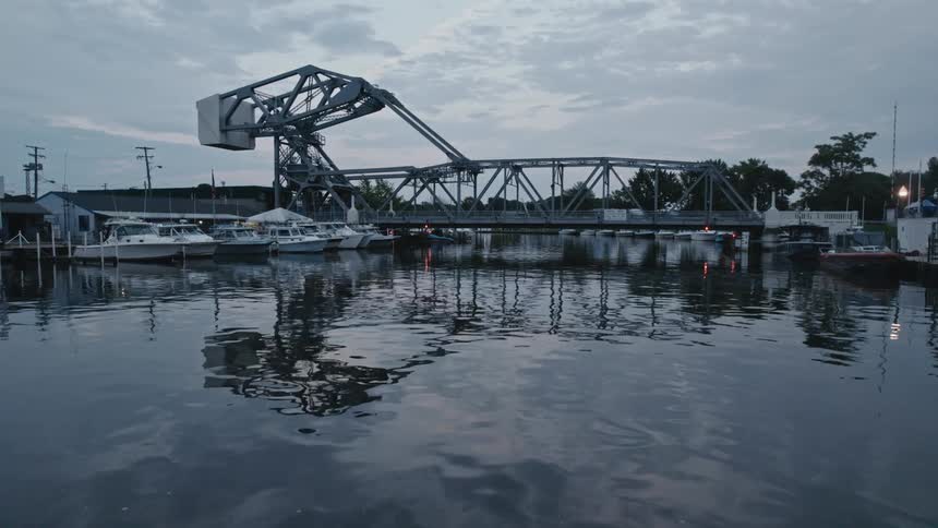 Boats sit docked on each side of the river while a car travels over the bridge