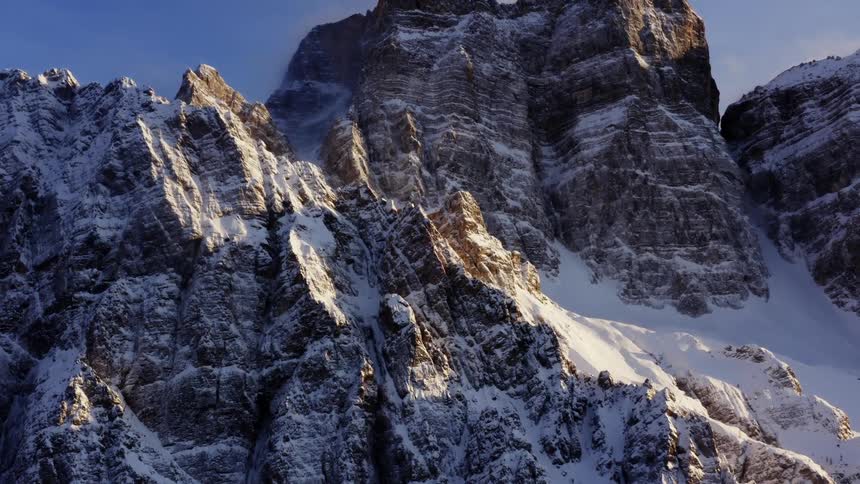 The sun shines on mountains and rock formations with a light snow covering