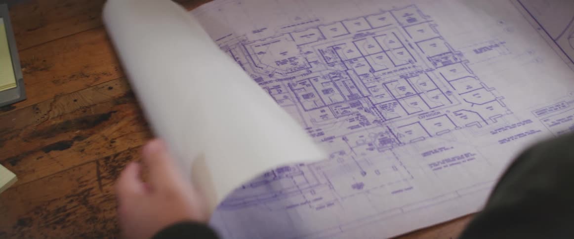 Man unrolls a diagram on top of a keyboard and a wooden table
