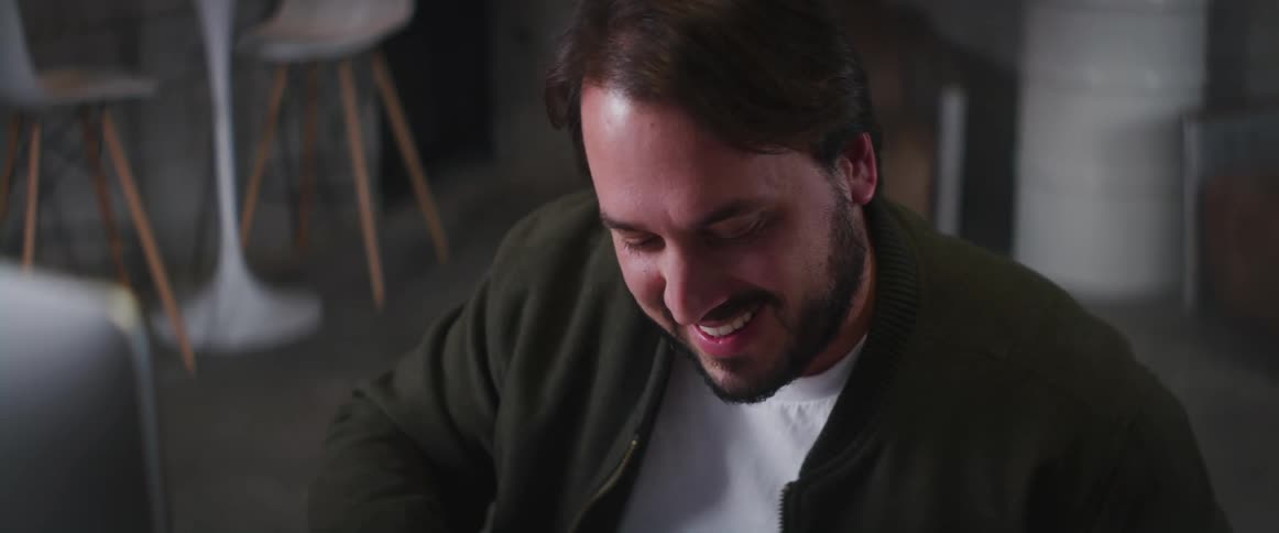 Man with beard green jacket and white shirt sitting at table works on paper while making video call