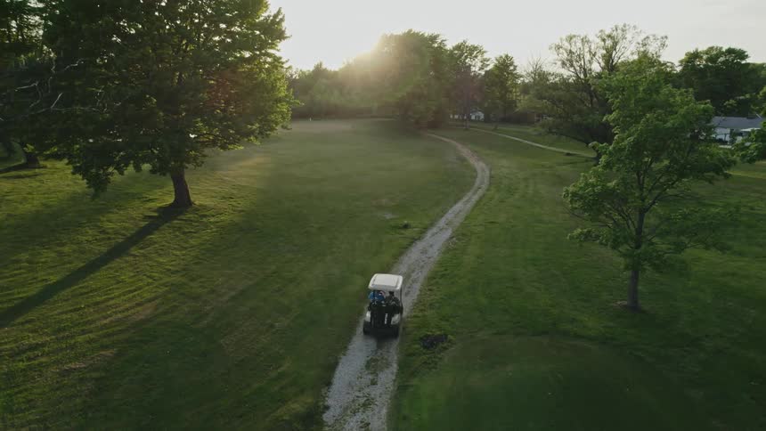 A pair of people ride a golf cart along a dirt road through a golf course
