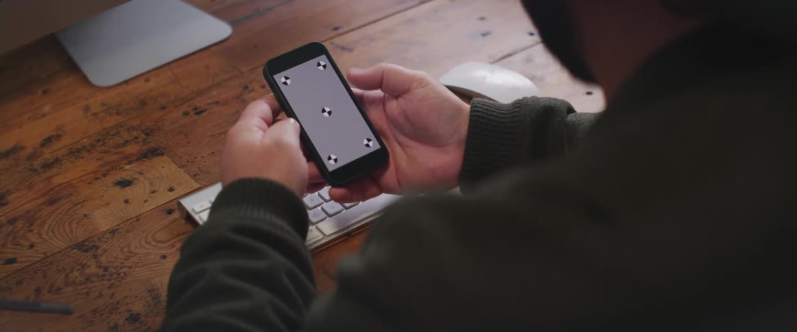 A man is sitting at a desk holding his phone with a gray screen and symbols