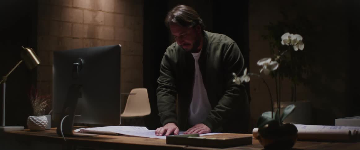 A man standing at his desk looking at blue prints and following the plans with his finger
