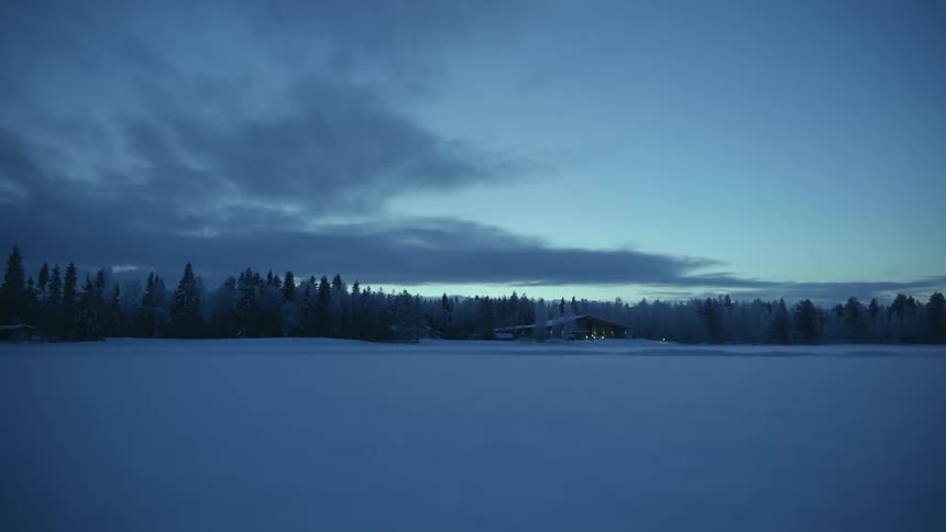 A snow covered field and a house near a forest in blue hour