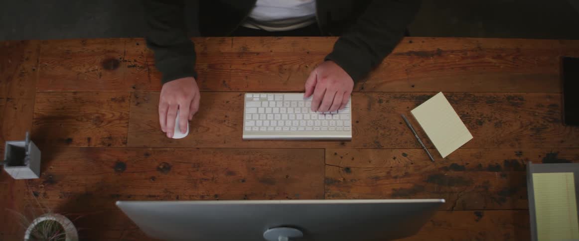 A man sits at a desk with computer and starts typing on the keyboard