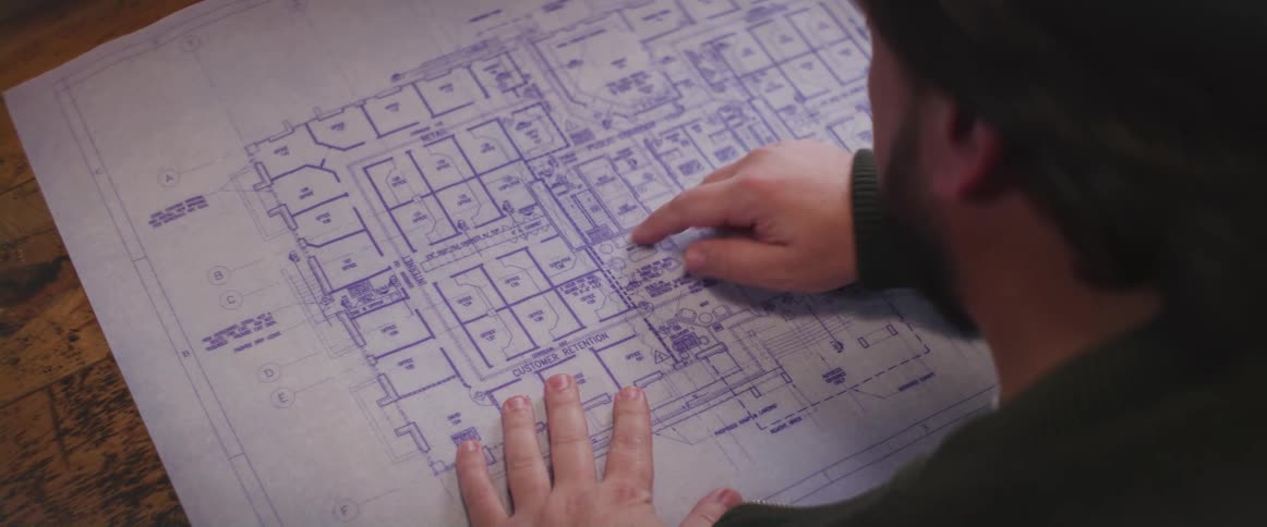 A man examines a blueprint before tapping a location with his finger