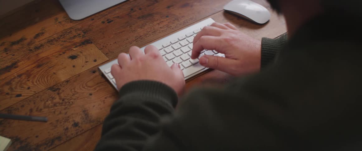 A man sitting and typing on a wireless keyboard