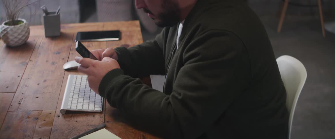 A man is sitting at a desk and texting on a phone