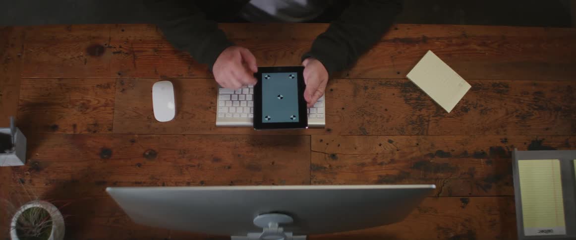 A person swipes and taps the screen of a computer tablet while sitting at a desk