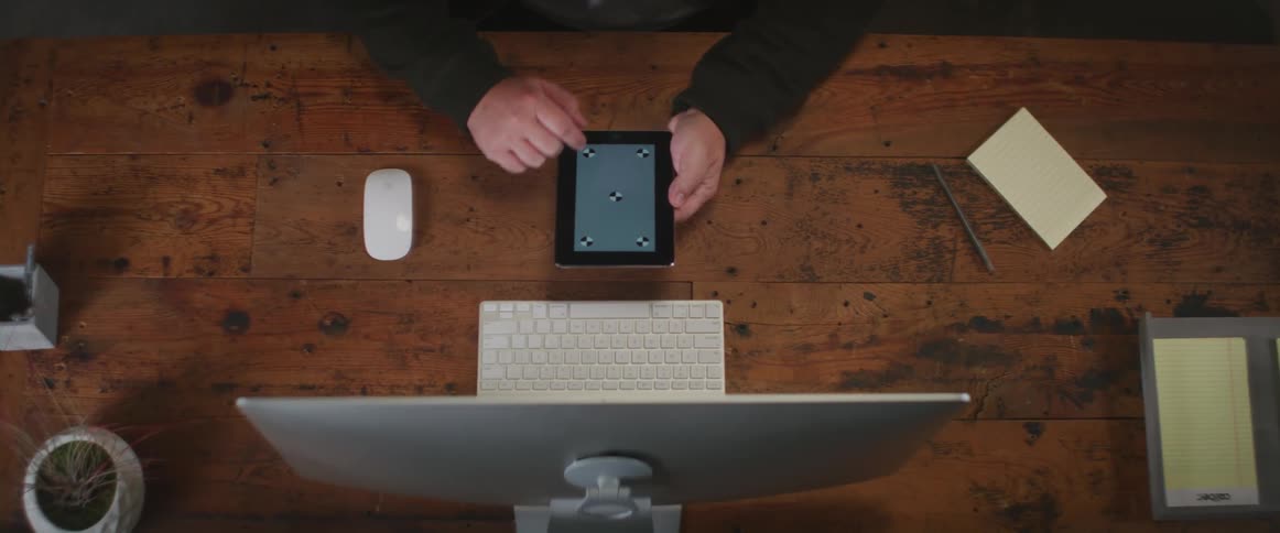 A person sitting at a computer desk swipes their finger across the screen of a tablet computer