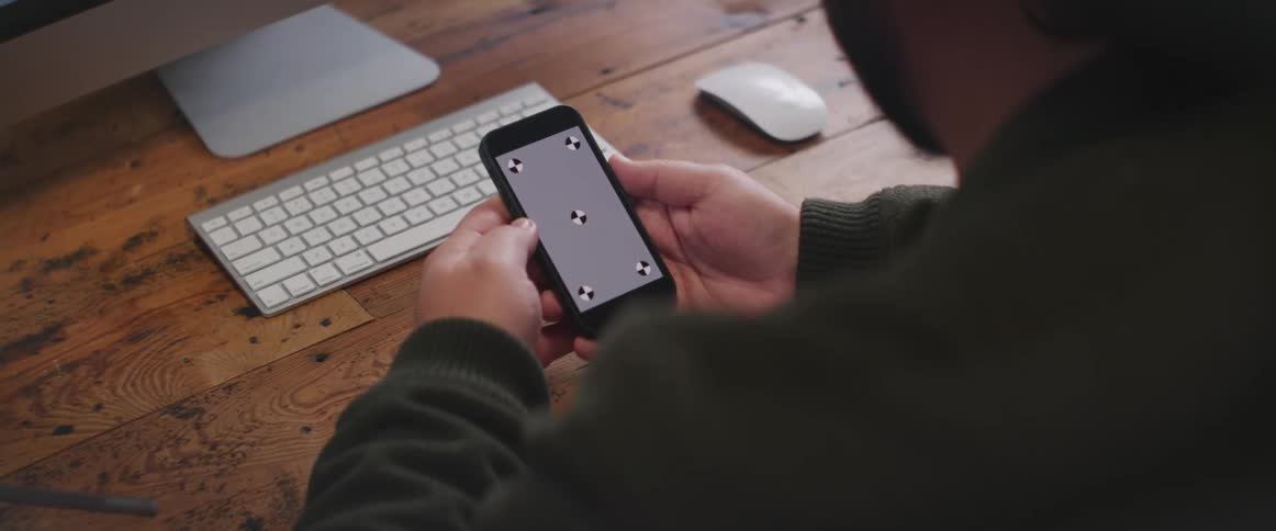 A man is sitting at a desk holding a cell phone and looking at a gray screen with symbols