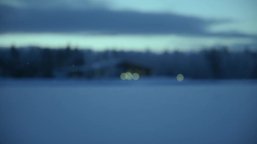 snowflakes falling in focus with forest cabin in background