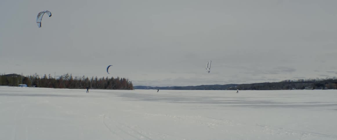 People snow kiting on a snow covered frozen lake