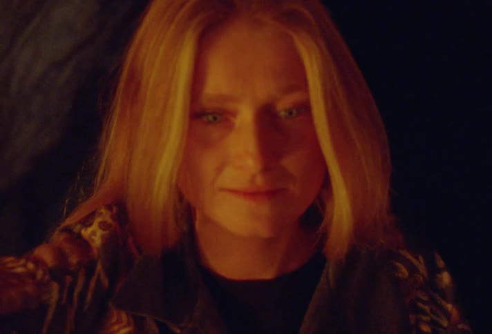 Blonde woman holding a gas lamp on her raised hand explores a cave