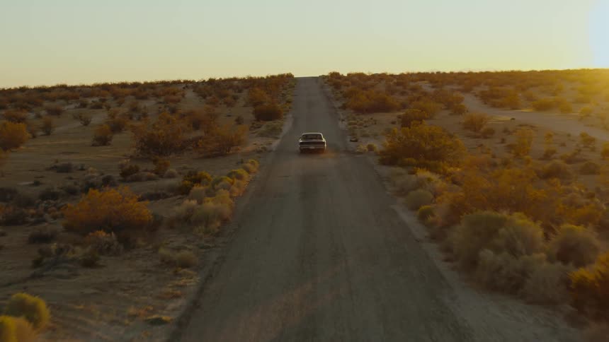 A car travels along a dusty road through badlands during the day