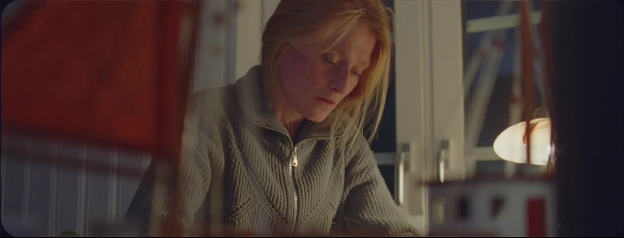 A woman sits at her desk and concentrates on what she is drawing until she crumples up the page in frustration