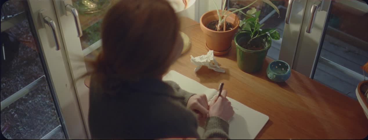 Blonde woman writing on a notepad over a desk at home at night caught on vintage film