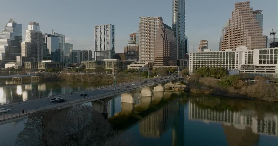 Aerial view of traffic moving on a bridge over a river in front of the city skyline at morning