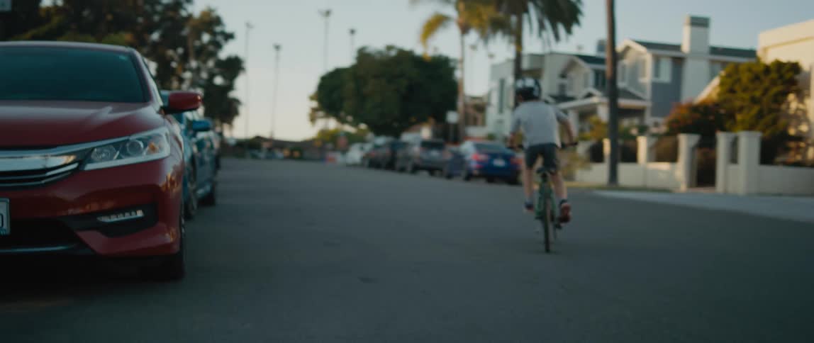 A child rides a bicycle down a road through a residential neighborhood during the day