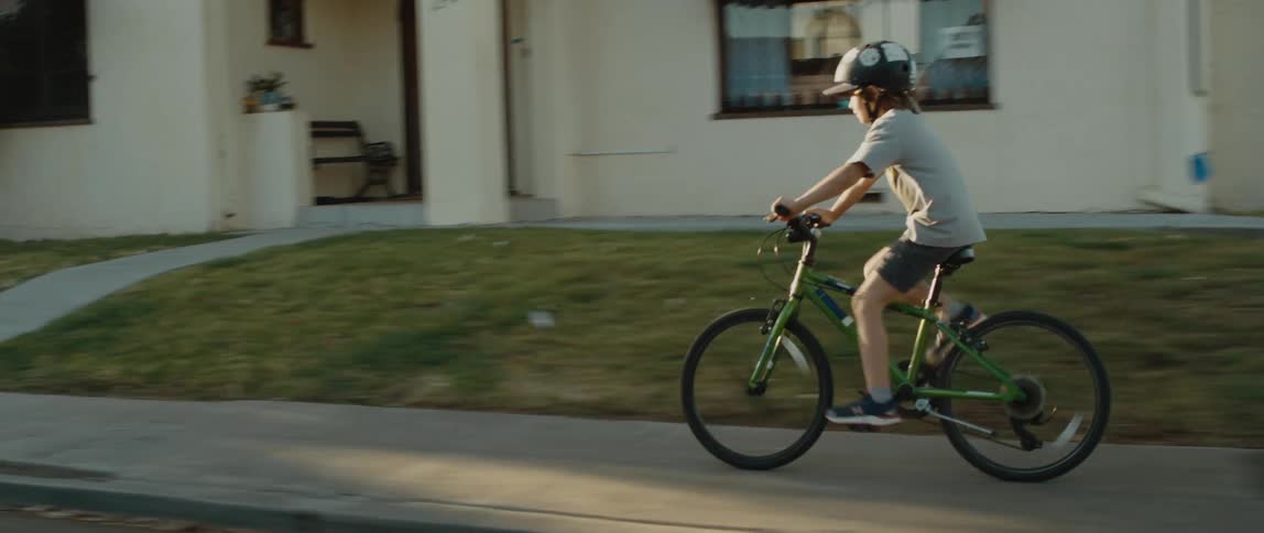 A young boy wearing a helmet rides his bicycle along a residential street