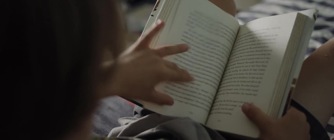 Young boy laying in bed reads a book in the morning