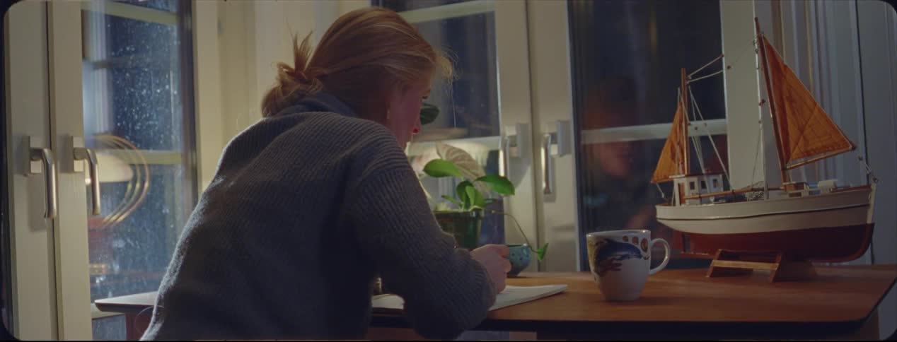 Blonde woman writing on a notepad over a desk at home at night caught on vintage film